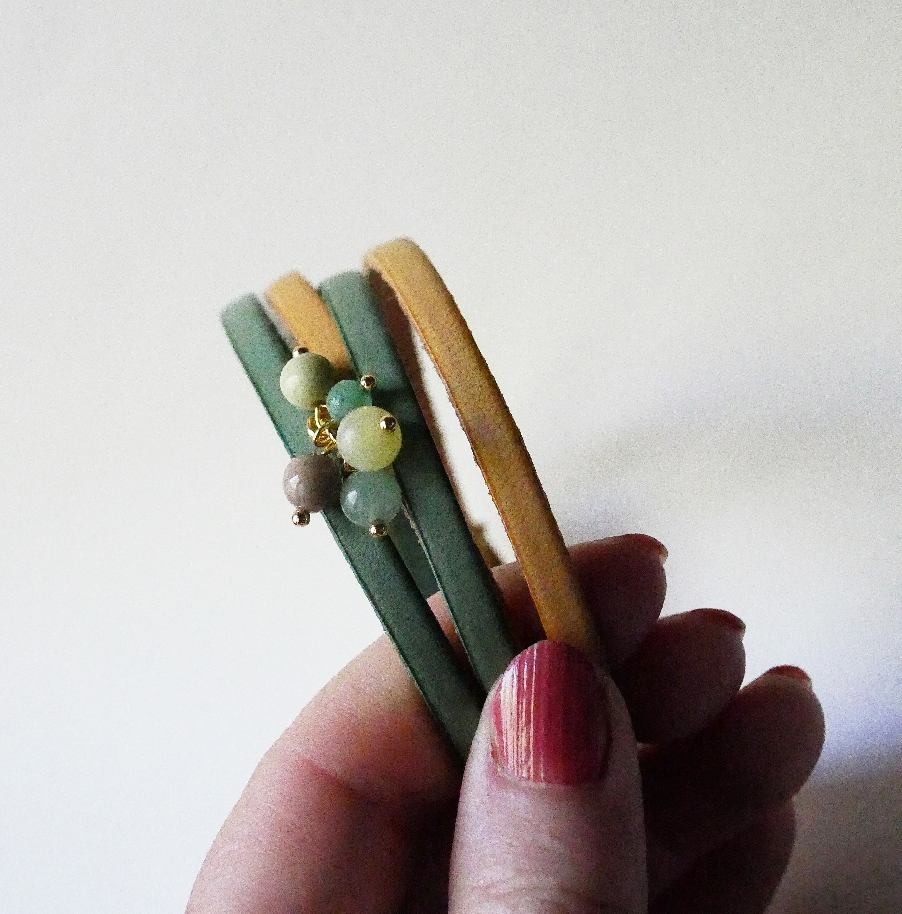 Dubbelt l&auml;derarmband dekorerat med mjuka gr&ouml;na p&auml;rlor och guldsp&auml;nne