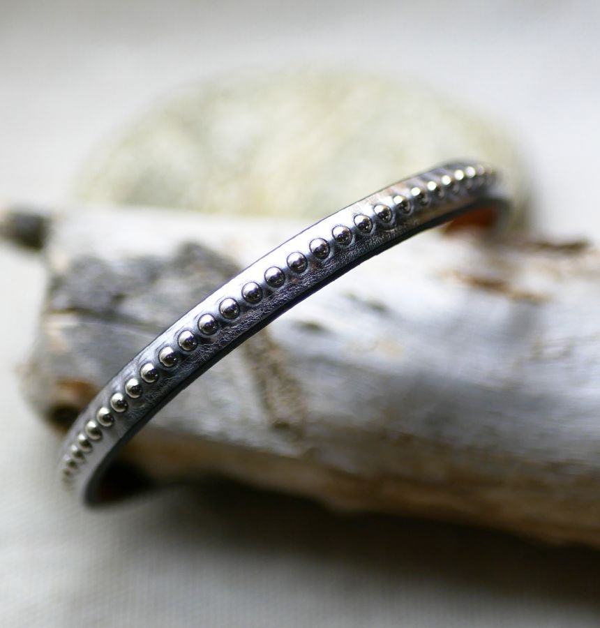 Kvinnoarmband i mörkgrått metalliskt läder med silverfärgade pärlor 