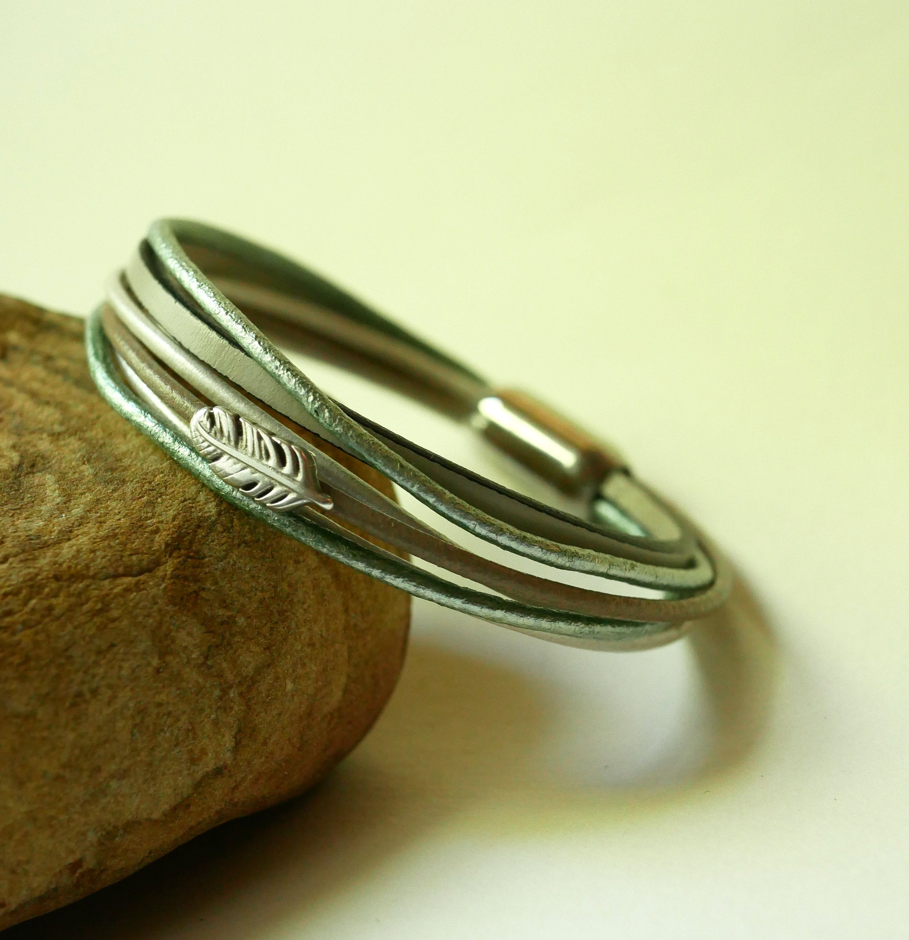 Armband i flera l&auml;derf&auml;rger i nyanser av beige, ljusgr&ouml;nt och p&auml;rlemor, dekorerat med en liten fj&auml;der