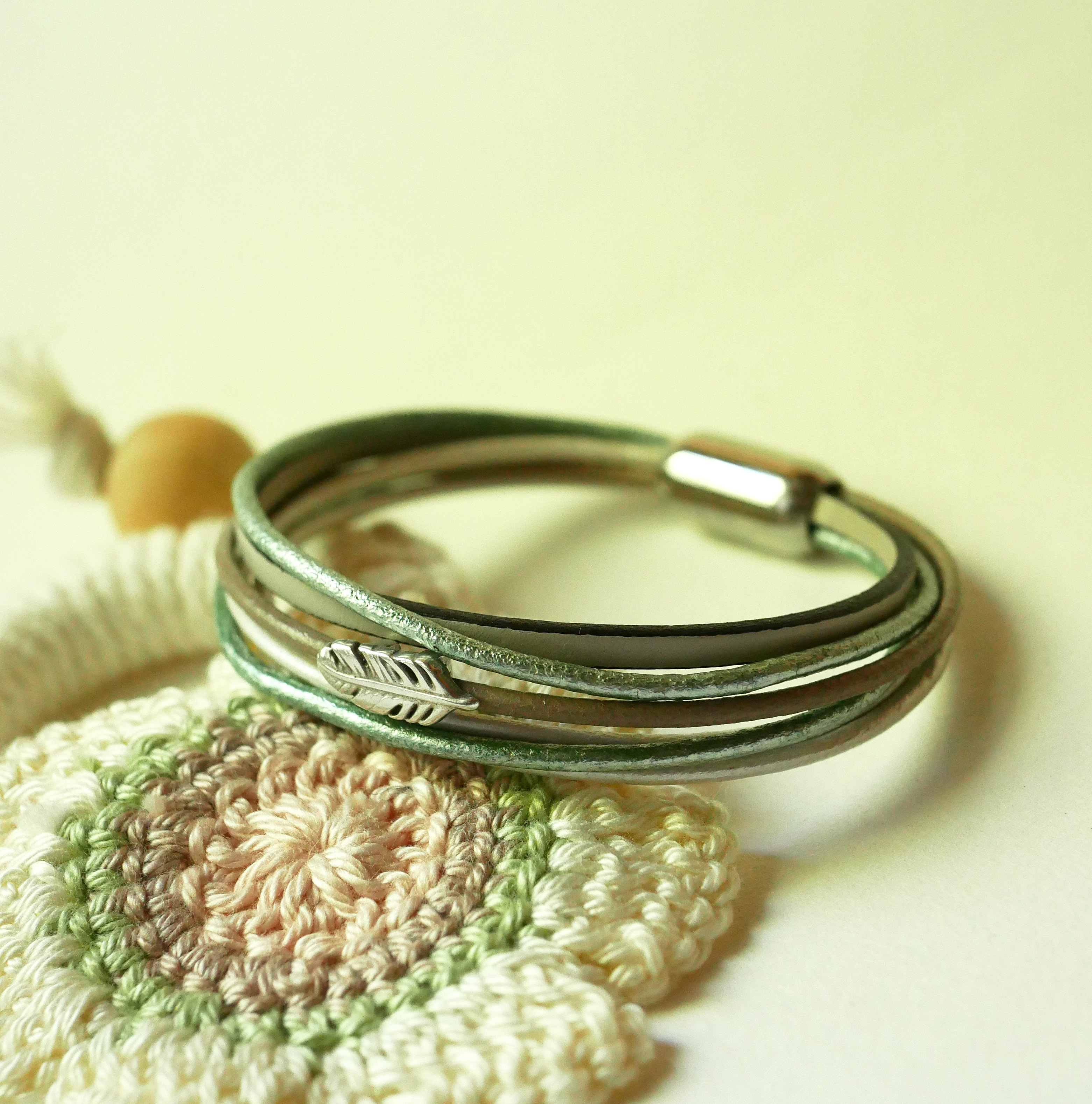 Armband i flera läderfärger i nyanser av beige, ljusgrönt och pärlemor, dekorerat med en liten fjäder