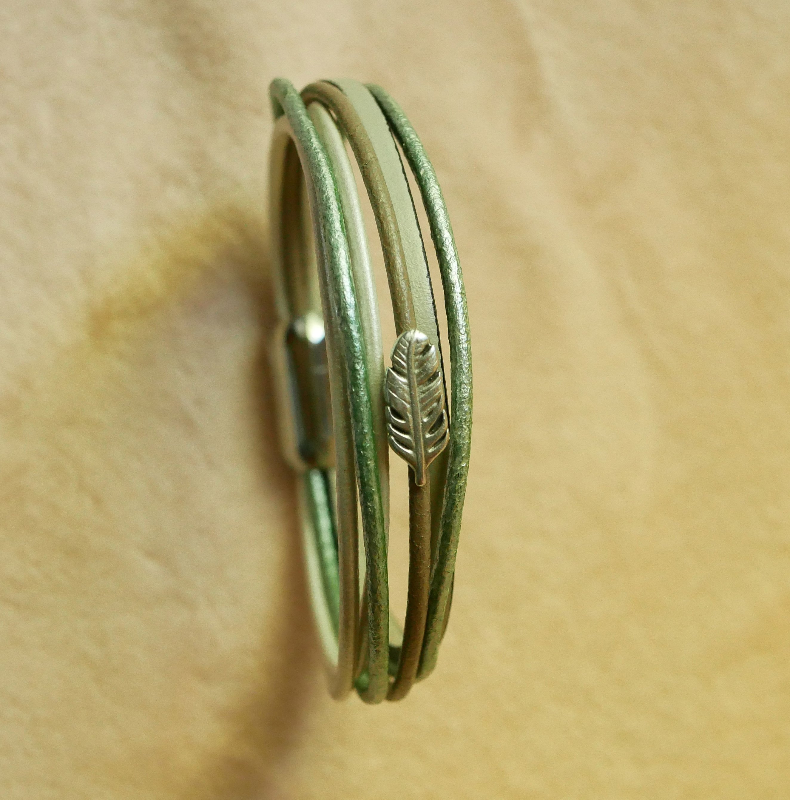 Armband i flera l&auml;derf&auml;rger i nyanser av beige, ljusgr&ouml;nt och p&auml;rlemor, dekorerat med en liten fj&auml;der