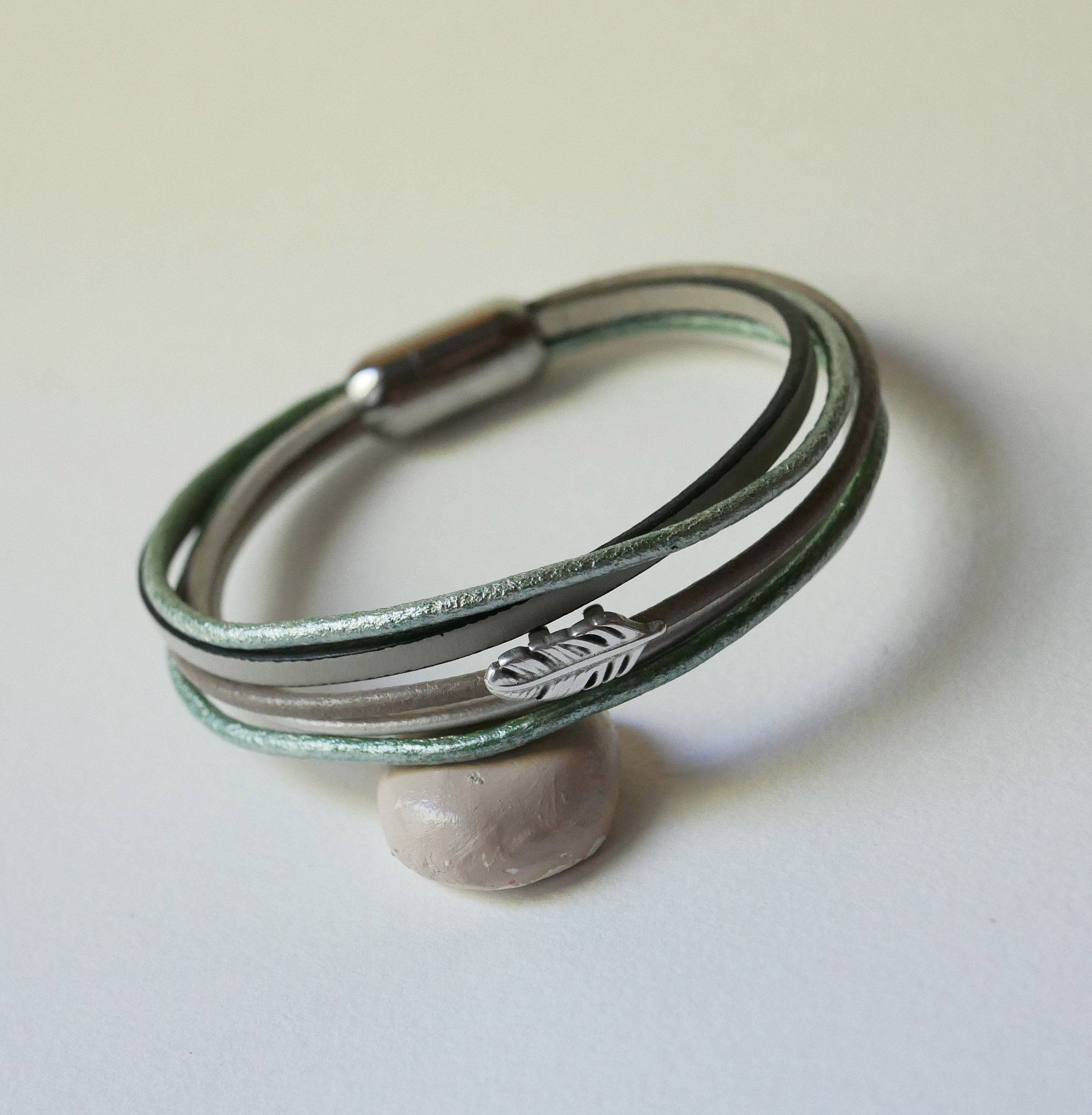 Armband i flera läderfärger i nyanser av beige, ljusgrönt och pärlemor, dekorerat med en liten fjäder