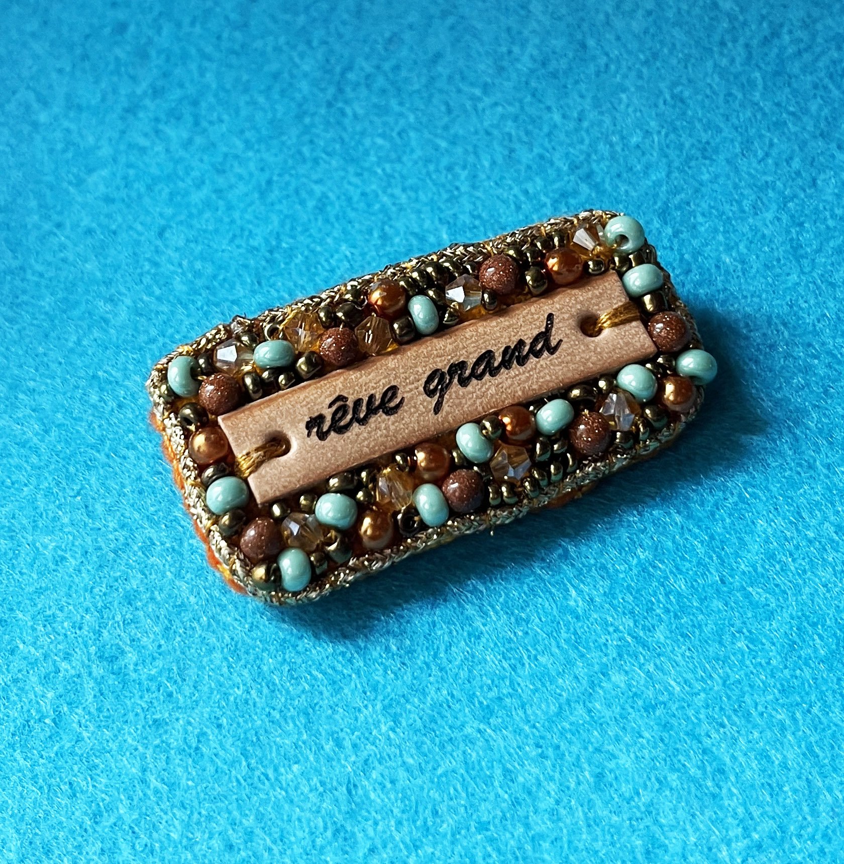 Broche en perles dorées à message en cuir gravé "rêve grand"