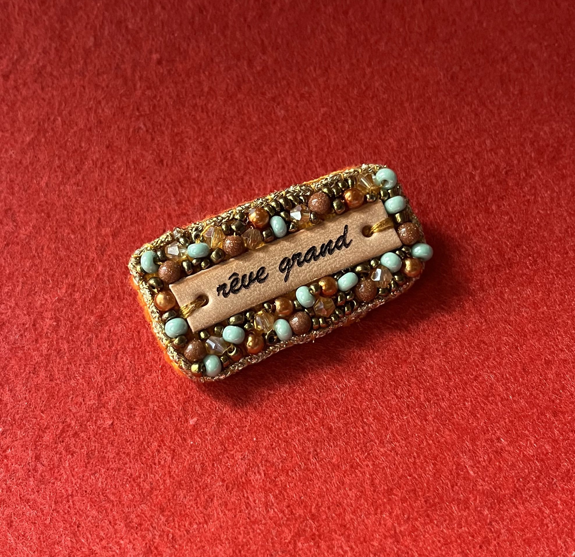 Broche en perles dorées à message en cuir gravé "rêve grand"