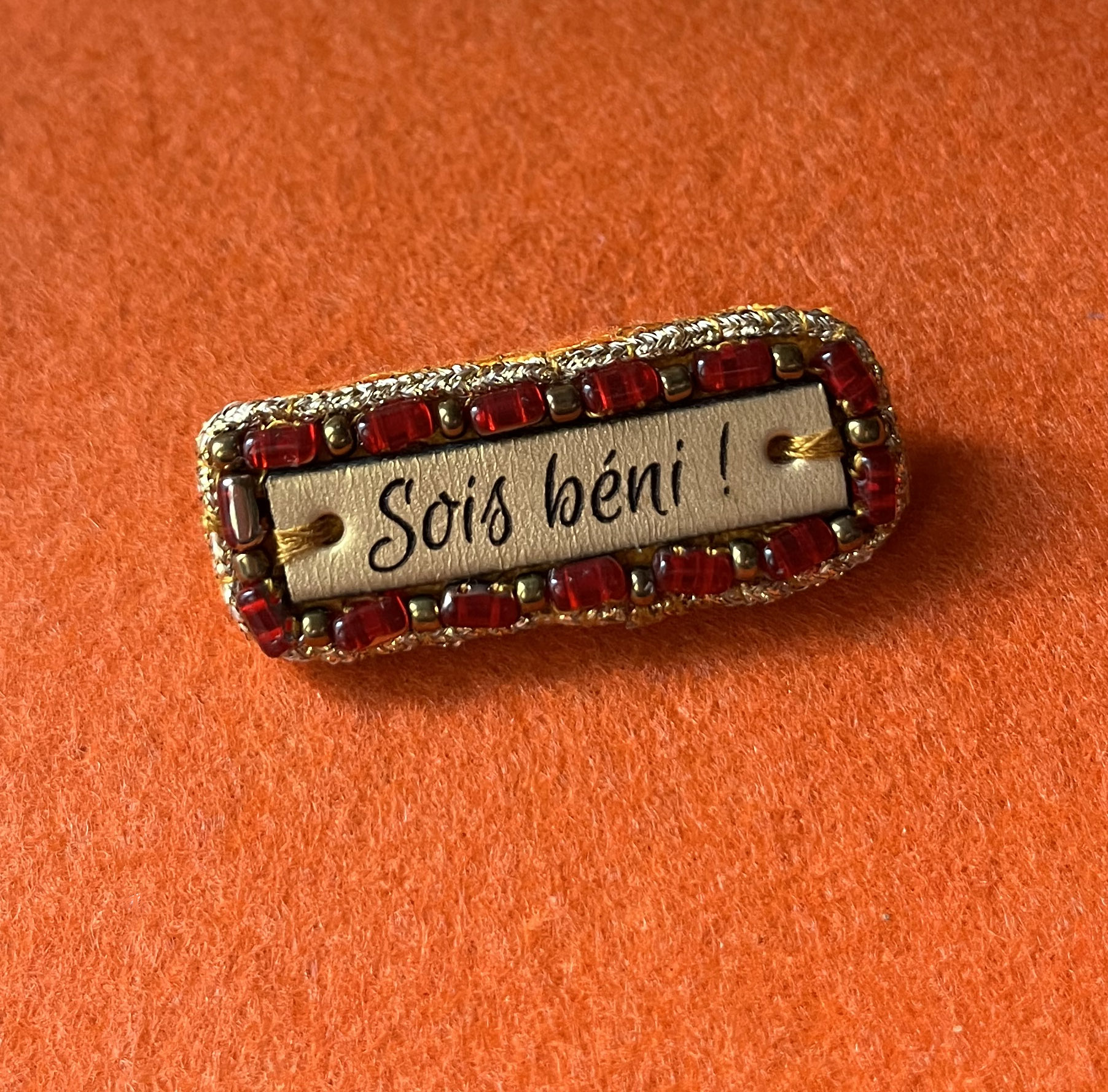 Broche à message en cuir gravé "sois béni" en perles rouges et dorées 