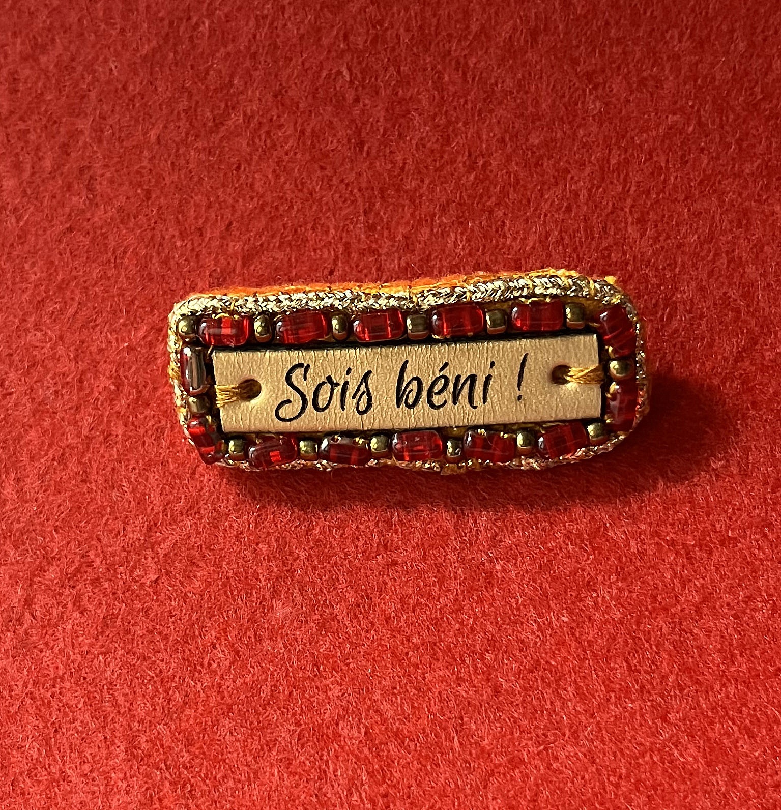 Broche &agrave; message en cuir grav&eacute; "sois b&eacute;ni" en perles rouges et dor&eacute;es 