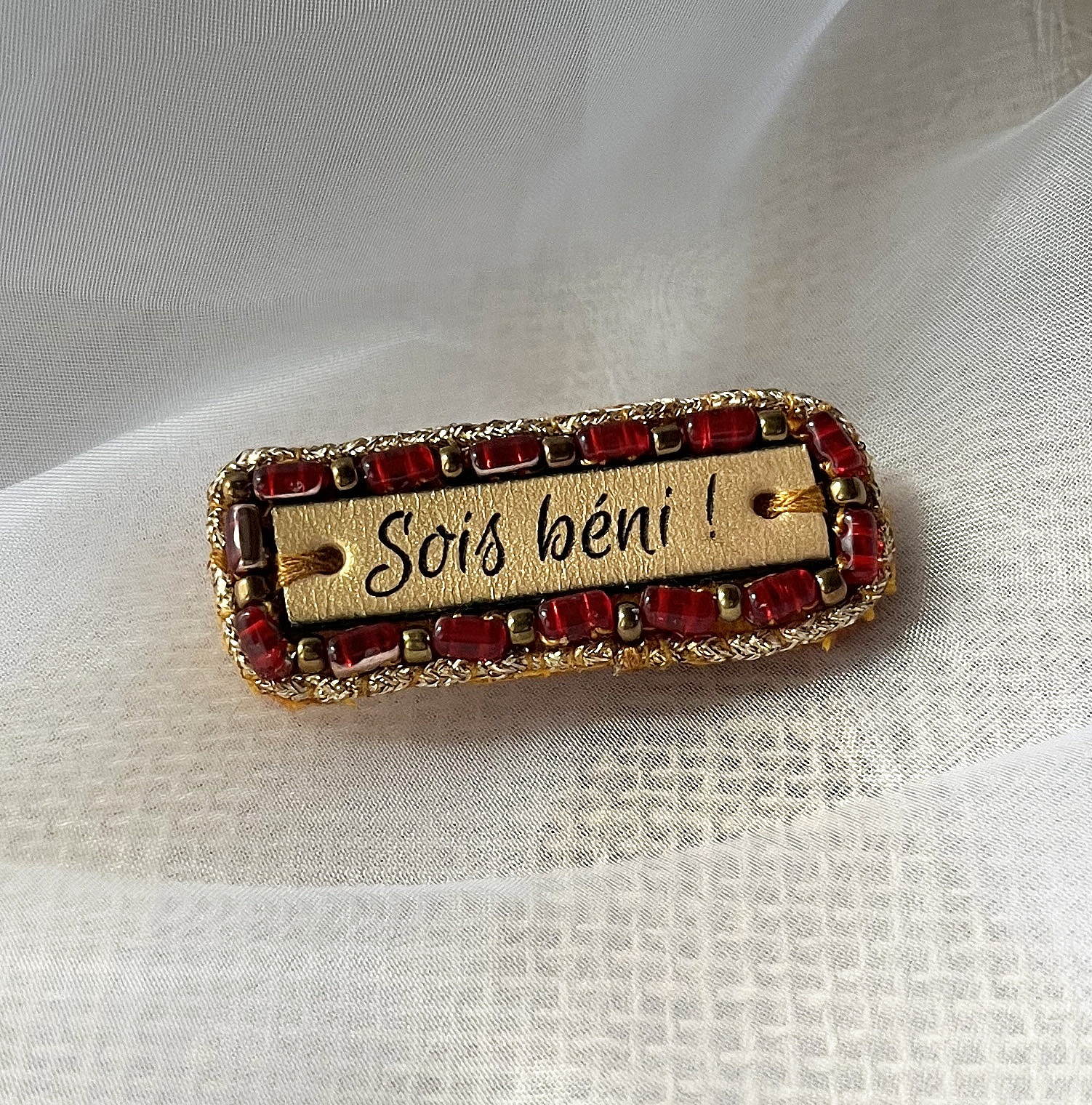 Broche &agrave; message en cuir grav&eacute; "sois b&eacute;ni" en perles rouges et dor&eacute;es 