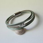 Armband i flera läderfärger i nyanser av beige, ljusgrönt och pärlemor, dekorerat med en liten fjäder